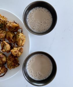 Two black mugs with vegan milky chai and half a white -late with pakora